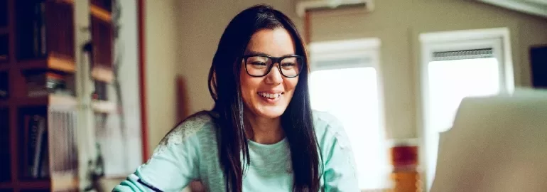 Smiling woman with glasses working on a laptop at home.