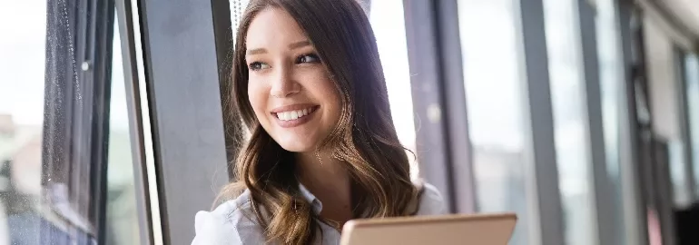 Woman smiling by a window with a tablet