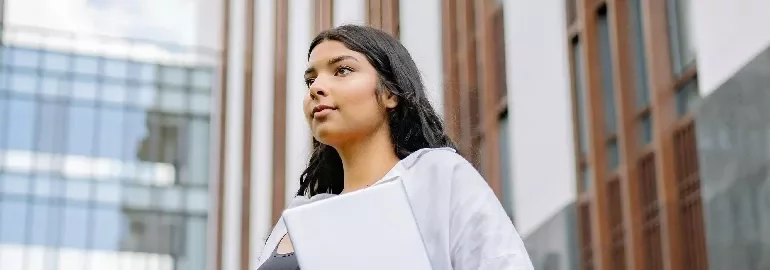 Person holding a laptop standing outside a modern building