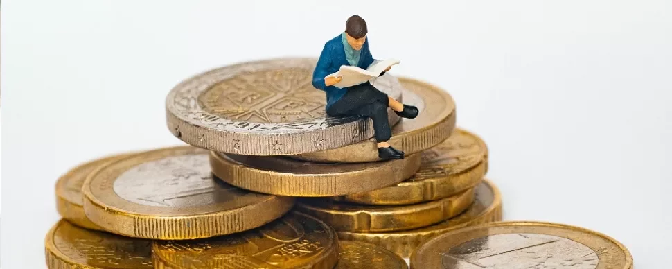 A male figurine sitting on a pile of gold coins reading a newspaper
