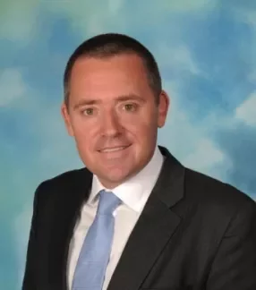 Person in a suit with a blue tie against a cloudy sky background.